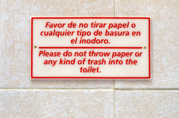 Bilingual Spanish- and English-language no trash in the toilet sign on the tiled wall of a hotel room bathroom