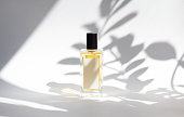 Bottle of essence perfume on white background with sunlight and shadows of leaves.