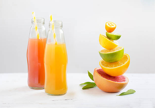 bottled citrus fruit juice with drinking straw along side with cut citrus fruits family stacked on white background. - natural juices stock pictures, royalty-free photos & images