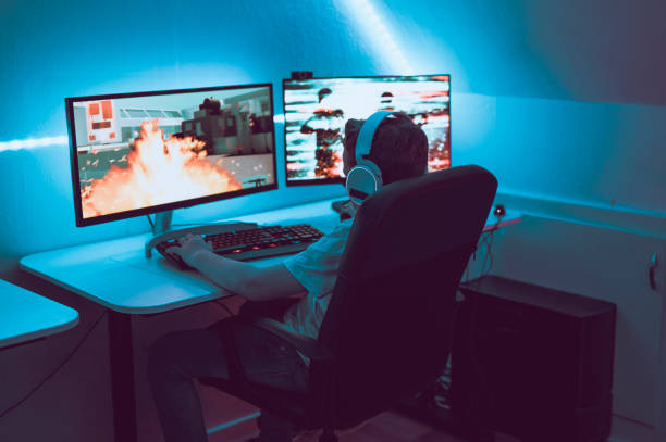 o menino joga o jogo video em linha e senta-se na frente de dois monitores de computador grandes - streaming live - fotografias e filmes do acervo