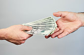 Business closeup of two hands exchanging dollars on grey background.