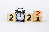 Business concept of 2022 new year. Turned a wooden cube and changed number 2021 to 2022. Black alarm clock. Beautiful white background, copy space. 2022 new year concept.