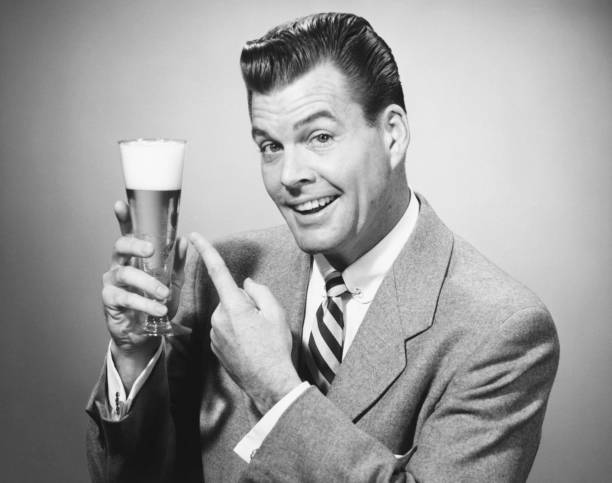 Businessman in full suit in studio pointing at glass of beer, (B&W), portrait