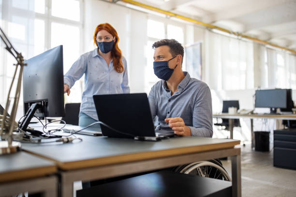 businessman working at his desk with female colleague standing by - professional software developer stock pictures, royalty-free photos & images