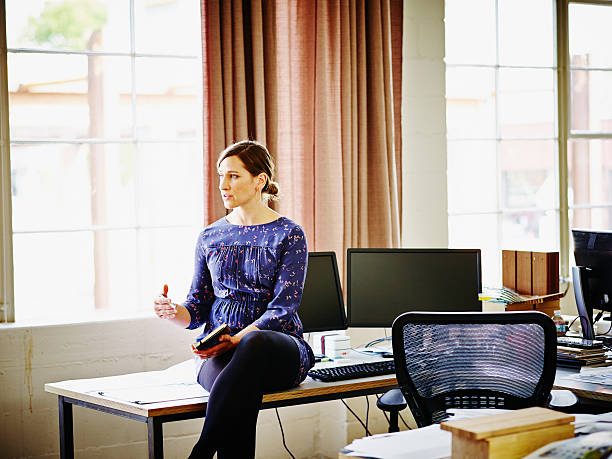 businesswoman seated on workstation in office - moveis de escritorio - fotografias e filmes do acervo