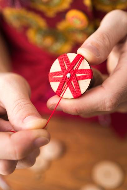 Button maker in third step of Posamentenknoepfe production holding wooden blank with vise and carefully wrapping red yarn in star pattern, unique regional handicraft
