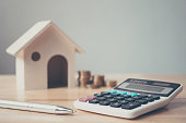 Calculator with wooden house and coins stack and pen on wood table. Property investment and house mortgage financial concept