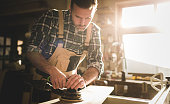 Carpenter at workshop polishes wooden board with a electric orbital sander