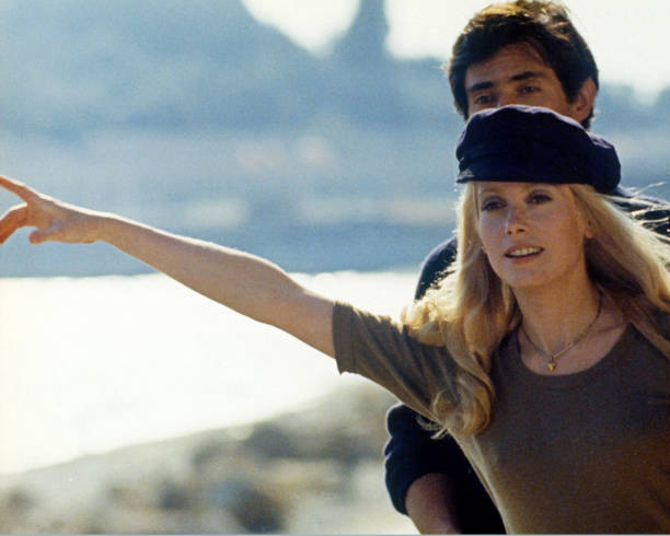 Catherine Deneuve, French actress, wearing a dark blue peaked cap and holding her right arm out as if hitchhiking, circa 1970.