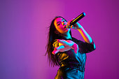 Caucasian female singer portrait isolated on purple studio background in neon light