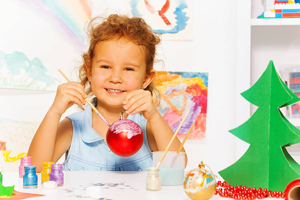 Cheerful girl painting New Year while sitting