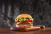 Cheeseburger with tomato and lettuce on wooden board