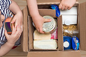 Children opening a food delivery box at home, online ordering. Grocery store delivery. Box full of food in concept donation boxparcel. Delivery during quarantine due to coronavirus COVID-19 disease