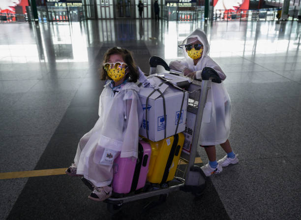 Chinese boy pushes his sister on a a luggage cart as they wear protective masks, sunglasses and raincoats after arriving on a flight at Beijing...