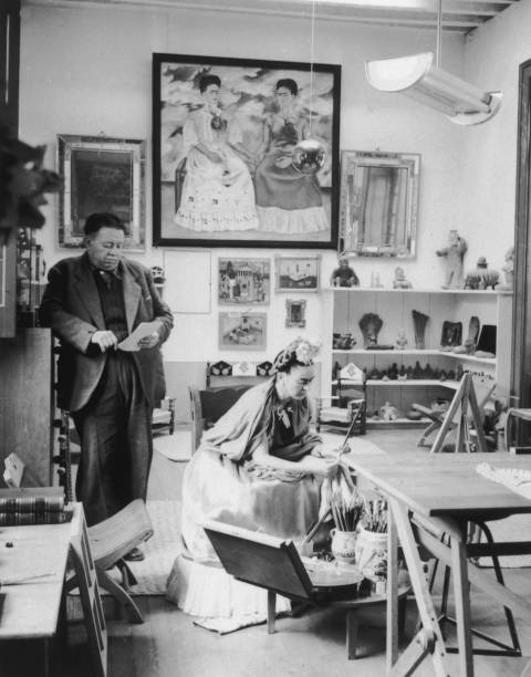 Married Mexican artists Diego Rivera and Frida Kahlo read and work in a studio. Kahlo's self-portrait, 'The Two Fridas' , hangs in the background...