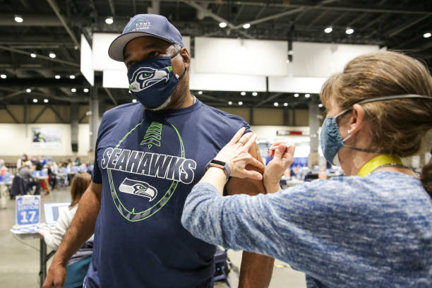 Cleveland Hughes wears Seahawks gear as he gets the Pfizer Covid-19 vaccine from Andrea Barnett during opening day of the Community Vaccination Site,...
