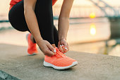 Close up of sporty woman tying shoelace while kneeling outdoor, In background bridge. Fitness outdoors concept.