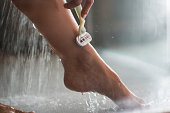 Close up of unrecognizable woman shaving her leg under the shower.