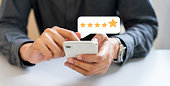 close up on businessman hand pressing on smartphone screen with gold five star rating feedback icon and press level excellent rank for giving best score point to review the service , technology business concept