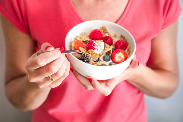 Close-up crop of woman holding a bowl containing Homemade granola or muesli with oat flakes, corn flakes, dried fruits with fresh berries. Healthy Breakfast