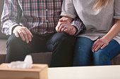 Close-up of a couple holding hands together while sitting on a couch during a therapy