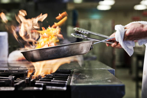 closeup of chefs hands holding a saute pan to cook food flambeing picture