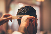 Close-up of hairstylist's hands cutting strand of man's hair