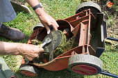 Close-up of hands fixing an overturned lawnmower with wrench
