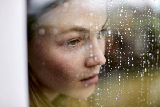 close-up of pensive young woman looking out of window - femme qui regarde par la fenetre photos et images de collection
