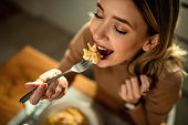 Close-up of young happy woman eating pasta at dining table.