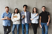 College students with books smiling to camera over grey wall