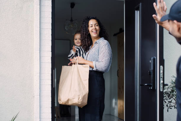 delivery man waving to smiling female customer carrying daughter picture
