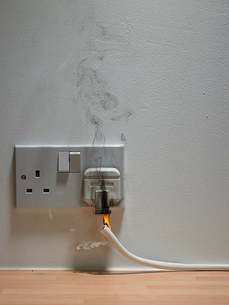 Electric plug in wall outlet with smoke and flame