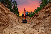 Excavator dig trench at forest area on amazing sunset background