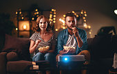 Family couple watching television projector at home on sofa