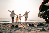 Family vacation holiday, Happy family running on the beach in the sunset. Back view of a happy family on a tropical beach and a car on the side.