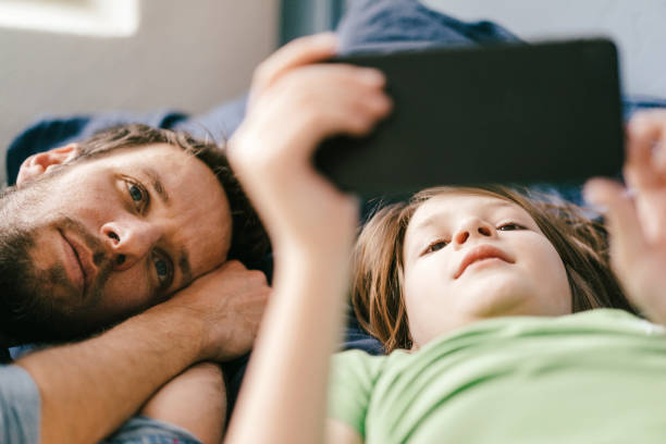father and son looking at smartphone together at home - streaming - fotografias e filmes do acervo