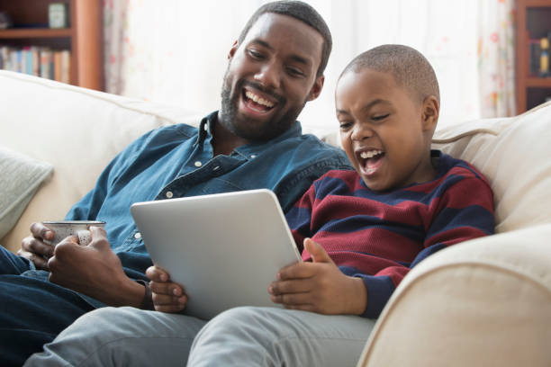father and son using digital tablet on sofa - streaming - fotografias e filmes do acervo