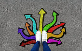 Feet and arrows on road background. Pair of foot standing on tarmac road with colorful graffiti arrow sign choices