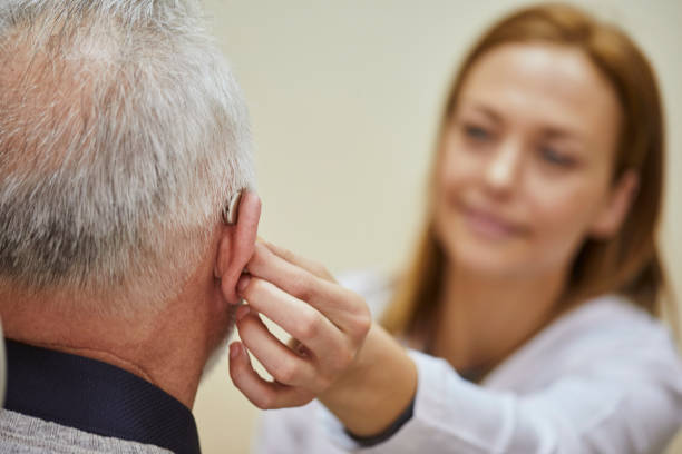 female doctor applying hearing aid to senior man's ear - angiologista - fotografias e filmes do acervo