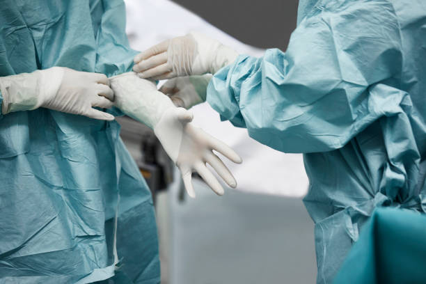 female doctor helping surgeon wearing glove - cirurgiões plásticos - fotografias e filmes do acervo