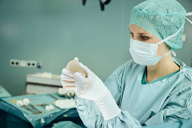 female surgeon holding up and checking silicone implant during surgery - prótese de silicone - fotografias e filmes do acervo