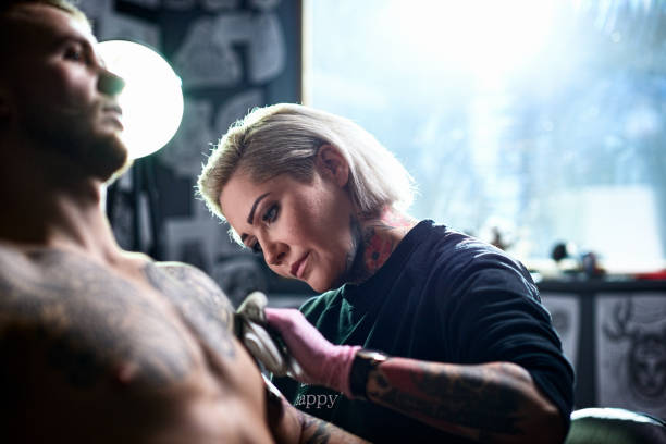 female tattooist applying tattoo to male customer picture