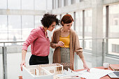 Female young architects with model of a house standing in office, talking.