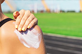 Fitness woman is applying sunscreen on her shoulder before training at the stadium. Protect your skin during sport activity