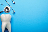flat lay with tooth model, stethoscope and sterile dental instruments arranged on blue backdrop