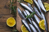 Fresh frozen sardines with lemon and rosemary on old, dark, wooden table