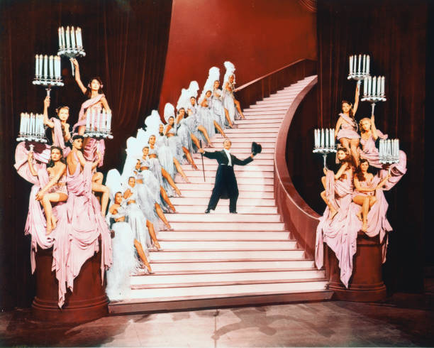 Gene Kelly , US actor and dancer, in top hat and tails, dancing on a flight of stairs lined with dancing girls in costume, in a publicity image...