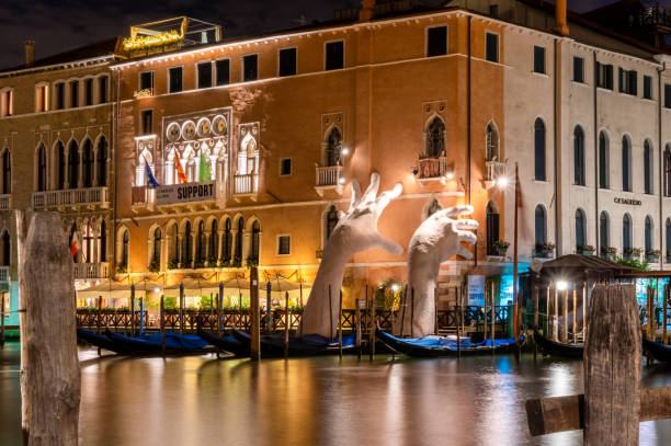 giant hands rise from the water of grand canal to support the building in venice at night - venice italy stock pictures, royalty-free photos & images