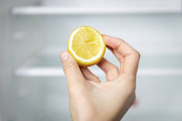 a girl's hand holds a lemon in front of an empty fridge. -  lemon in fridge stock pictures, royalty-free photos & images